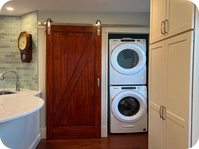 Dark wood sliding barn door beside stacked white washer/dryer; pale green tile backsplash.