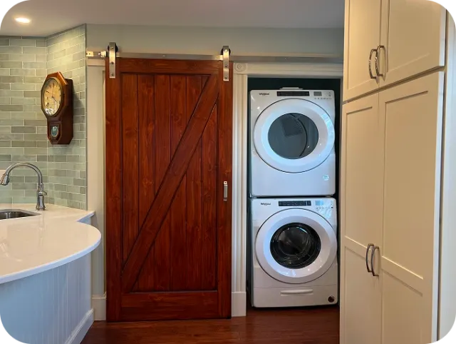 Dark wood sliding barn door beside stacked white washer/dryer; pale green tile backsplash.