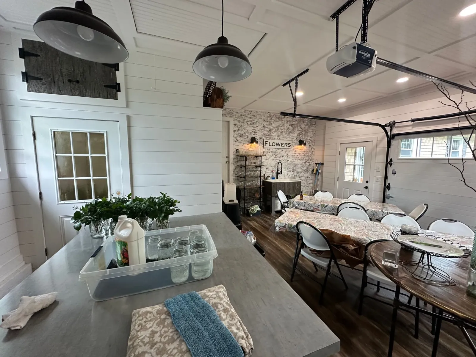 Rustic dining space with long table set for an event, white decor, hanging lights, and exposed brick wall