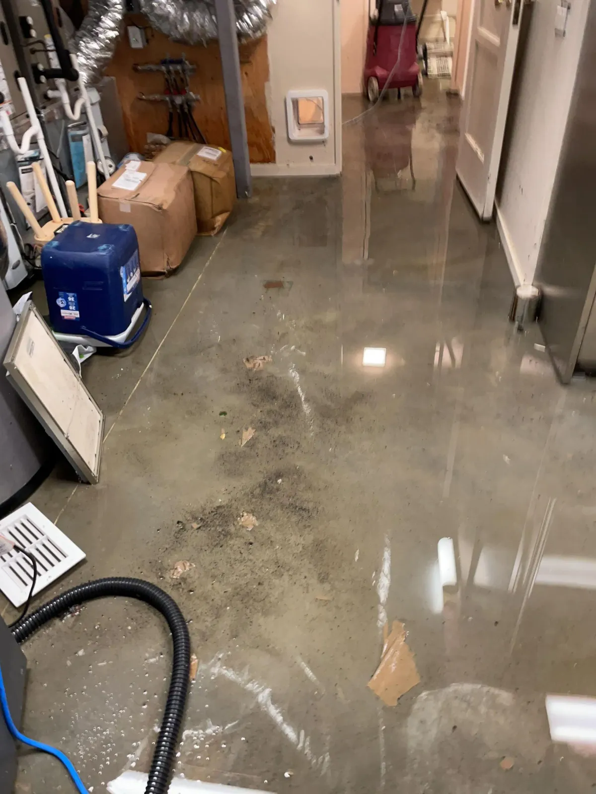 Flooded basement utility room with standing water, debris, and reflections on the floor