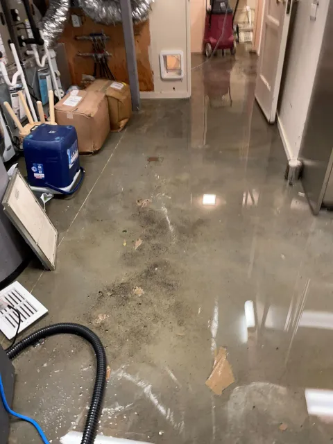 Flooded basement utility room with standing water, debris, and reflections on the floor