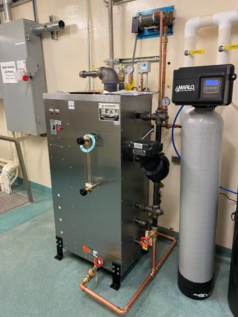 A stainless steel boiler with pipes and a water softener in a utility room.