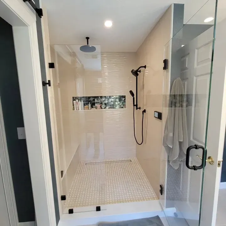 Bright modern shower with glass doors, white tile, and a black rainfall showerhead.