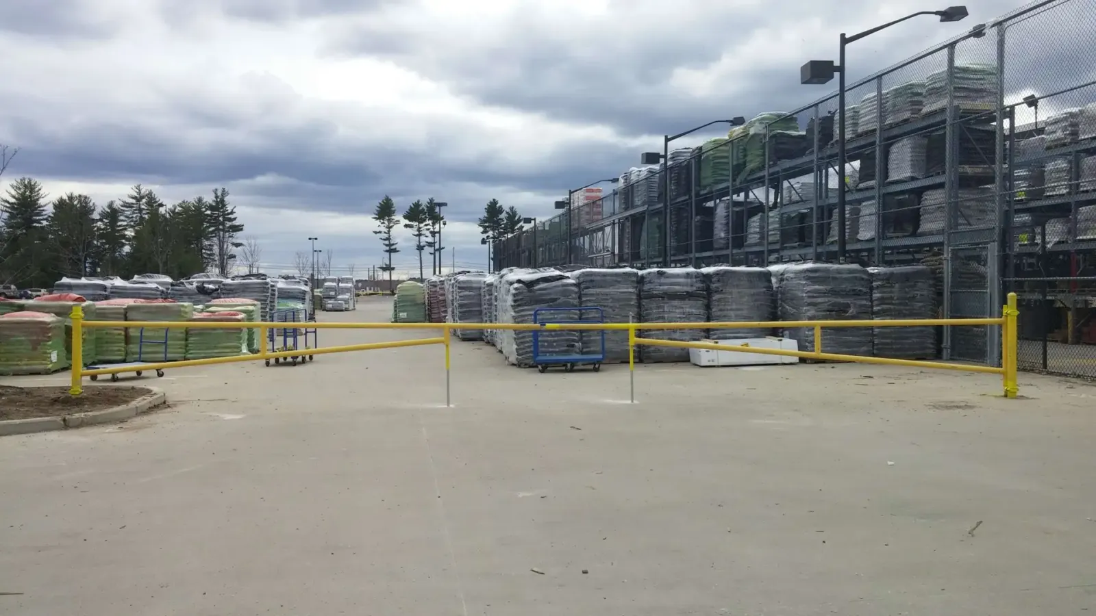 Olympic Fence Co. yard in West Newbury with chain-link fencing and stacked materials, showcasing quality fencing products and a lifetime workmanship warranty.