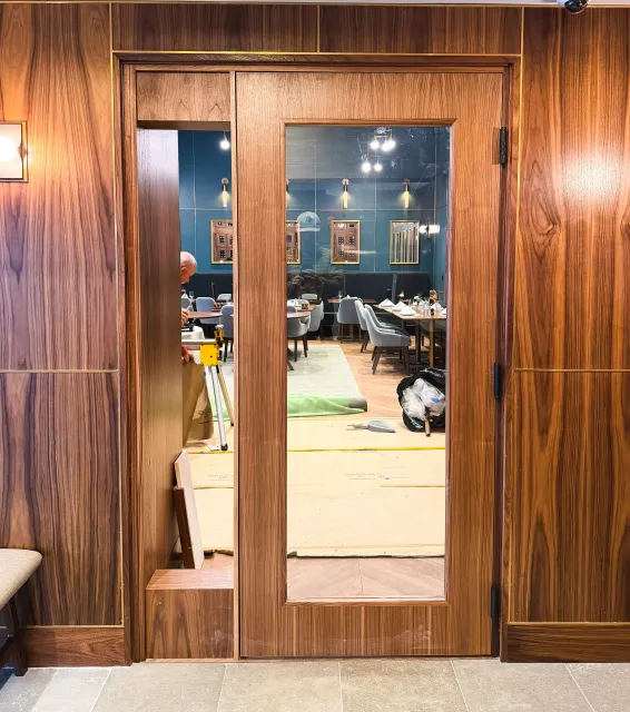 View through a glass door into a restaurant with wooden walls, blue walls, and several tables set for dining.