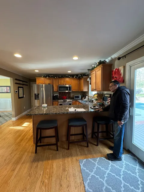 Kitchen with wood cabinets and granite island, with a person standing by the counter near sliding glass doors.
