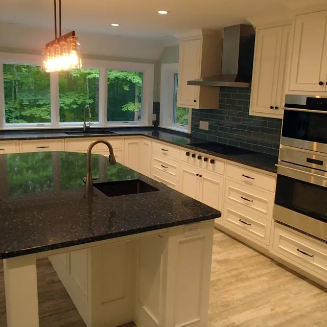Modern kitchen with white cabinets, dark granite countertops, and a blue tile backsplash.