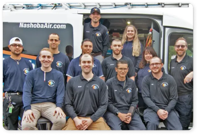 A group of twelve people in matching uniforms pose in front of a Nashoba Air vehicle.