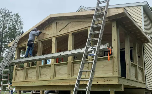 A worker on a ladder adds finishing touches to a wooden structure under construction.
