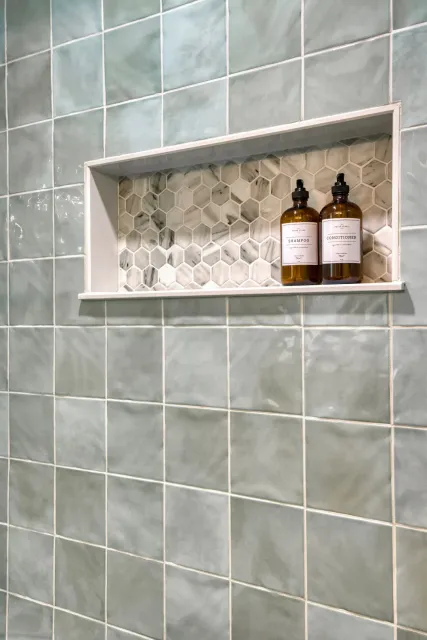 Tiled shower wall with recessed shelf holding two amber soap bottles.