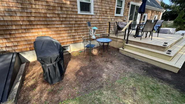 Backyard patio with grill, table, chairs, and wooden deck.