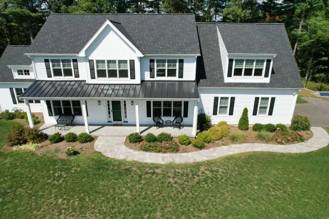 White suburban two-story house with gray roof, front porch, and a large green lawn