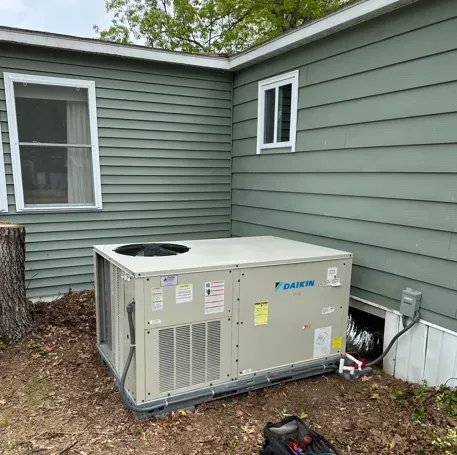 Outdoor HVAC unit beside a green house wall and white-trimmed windows