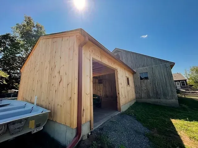 Wooden garage with open doorway beside a weathered shed on a sunny day