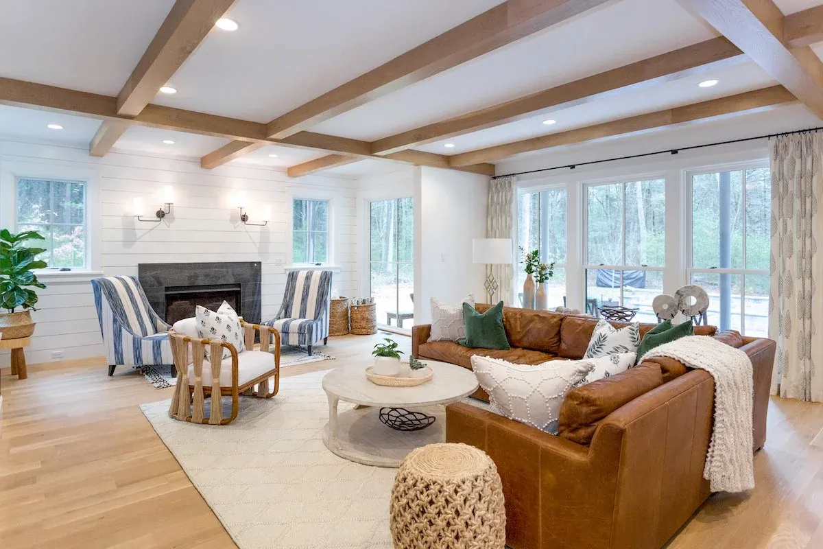 Living room with large fireplace and exposed wooden beams on the ceiling, decorated in neutral beiges, whites and blues