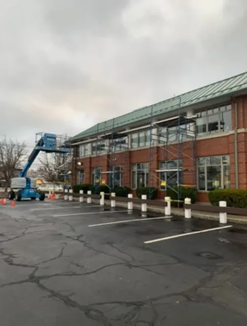 Brick office building with a blue cherry picker beside a wet parking lot on an overcast day