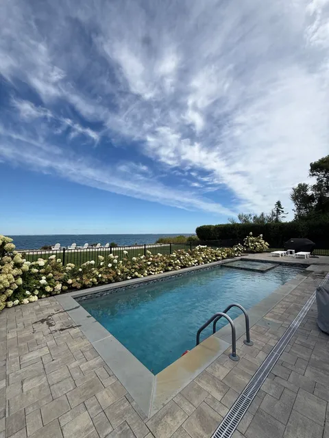 A pool and spa edged with white hydrangeas, with a view out over the water