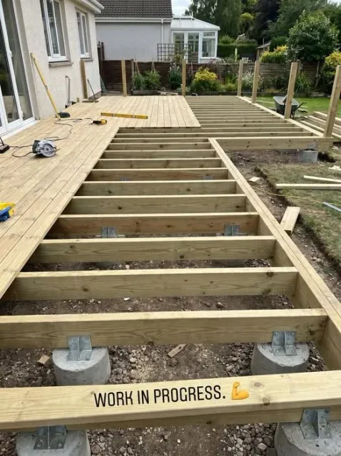 Deck framing under construction showing pressure-treated joists on concrete footings in a backyard