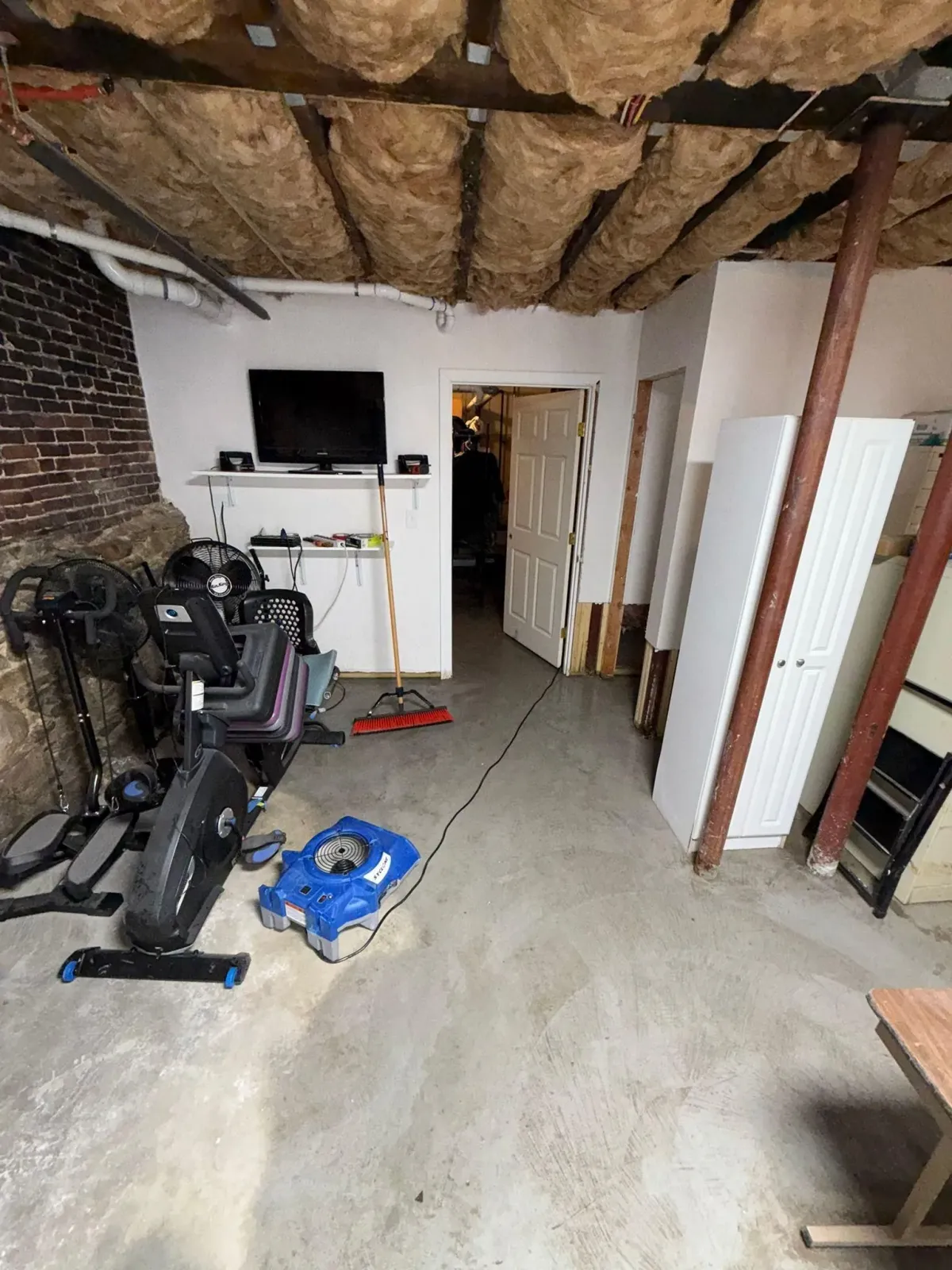 Basement home gym with exercise machine, exposed ceiling, and renovation tools on concrete floor