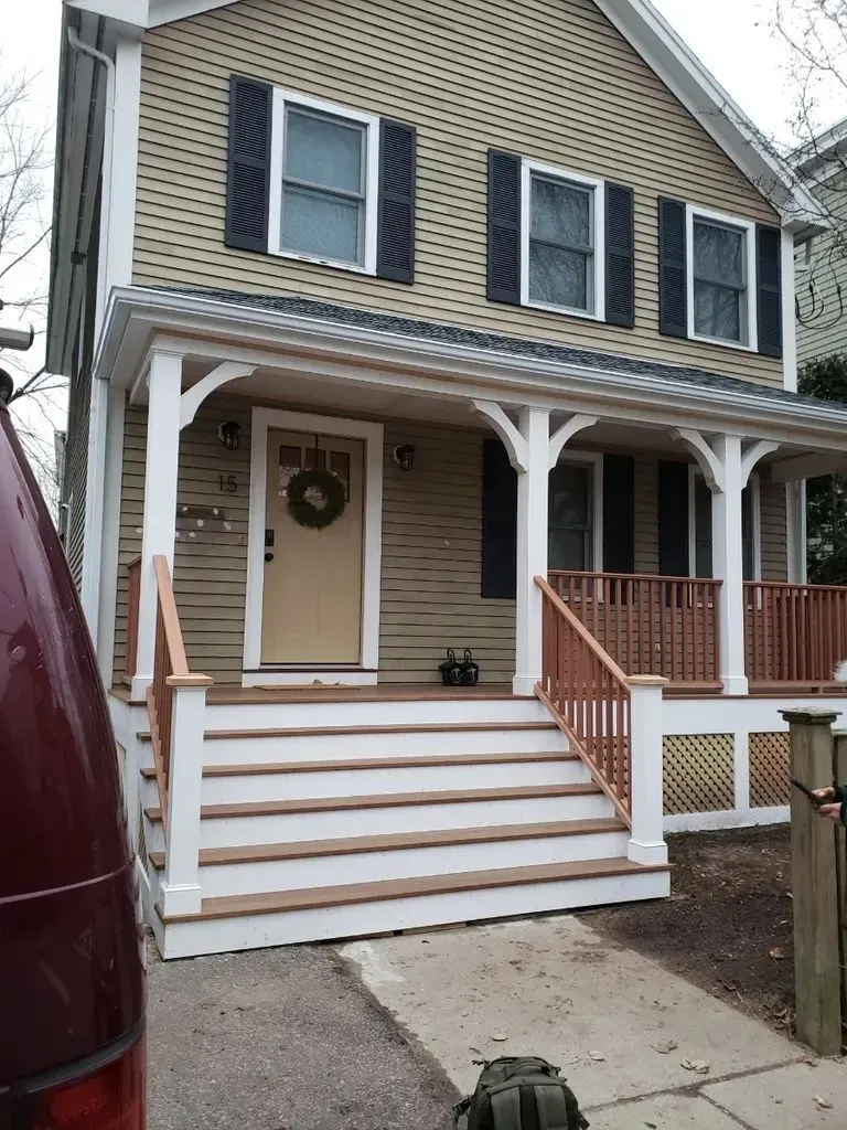 Two-story house with a front porch, white stairs, beige siding, and dark shutters