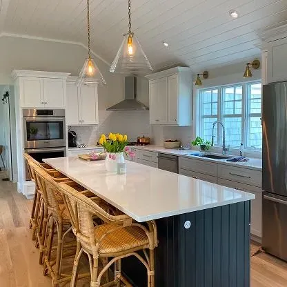 Bright kitchen with white cabinets, large island, wicker stools, pendant lights, and a window over the sink.