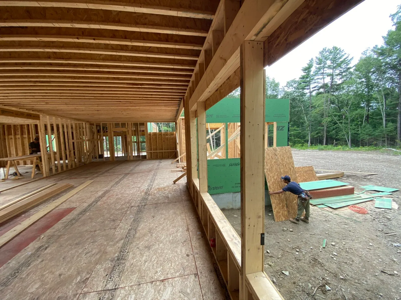 Construction workers building a wooden framework for a house, with trees in the background.