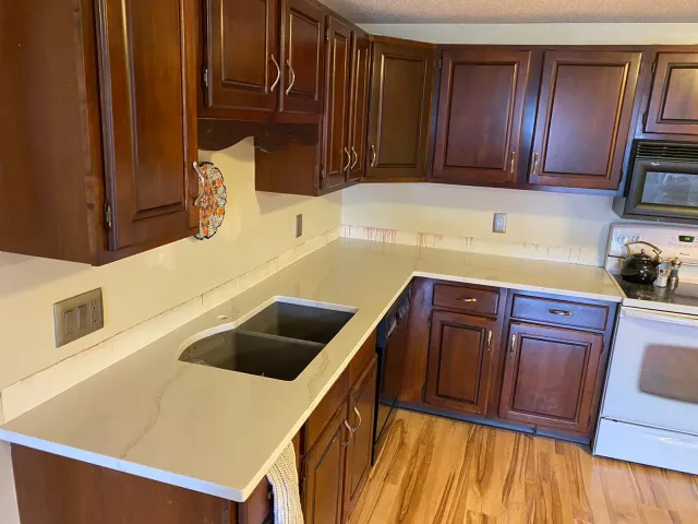 A kitchen with wooden cabinets , a sink , stove and microwave.
