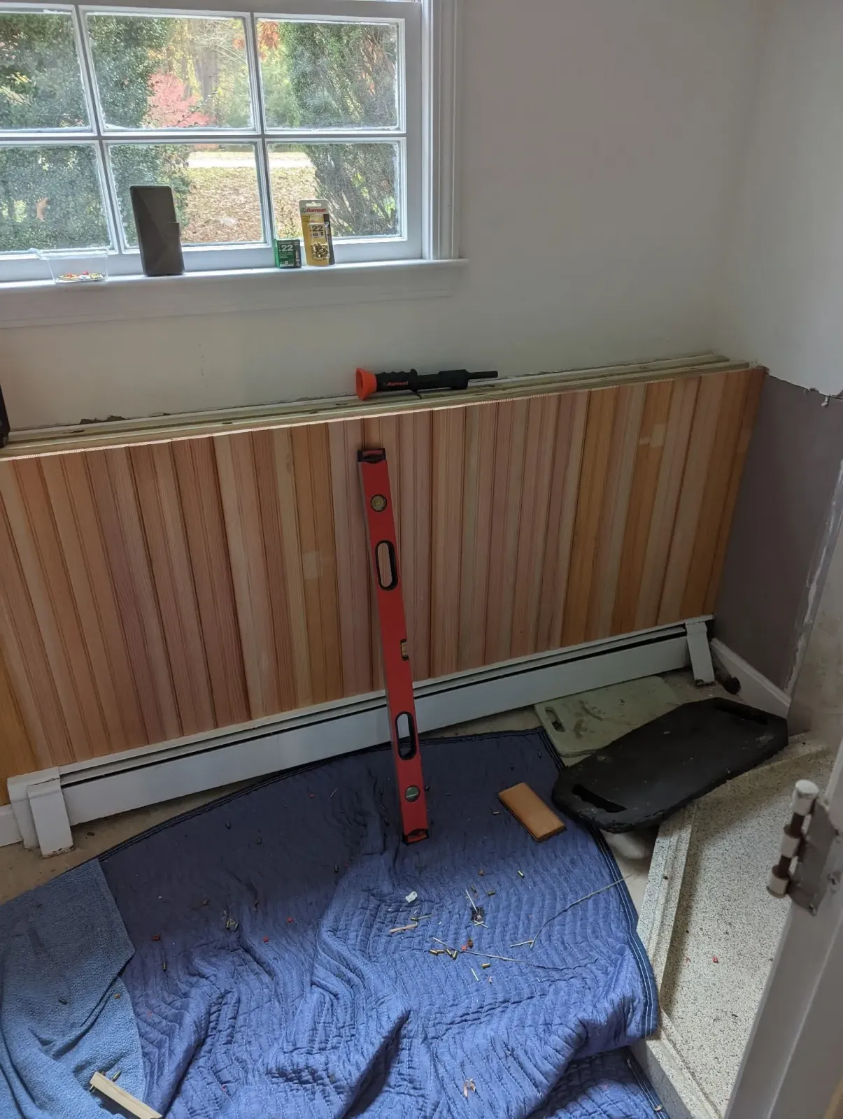 A red level is sitting on the floor next to a wooden radiator.