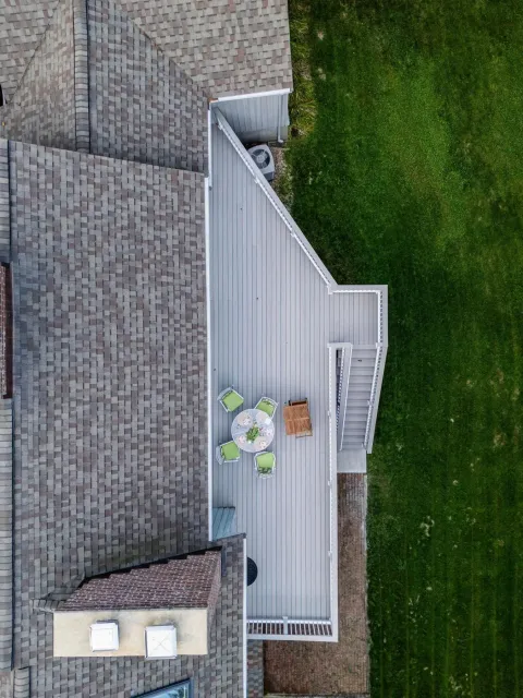 Overhead view of a house with a gray deck, outdoor furniture, and green lawn.