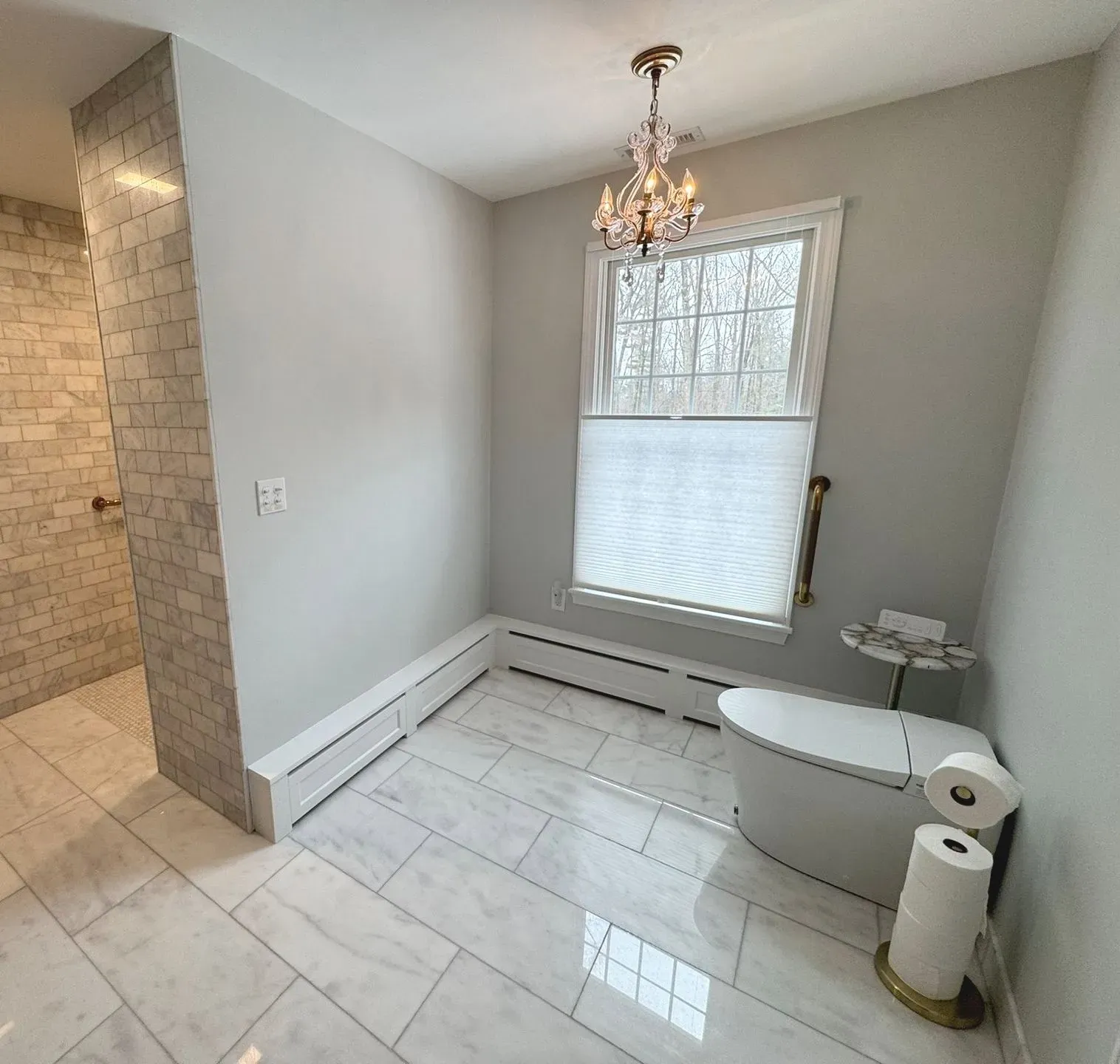 Small bathroom with white tile, toilet, window, chandelier, and a raised tub or shower area.