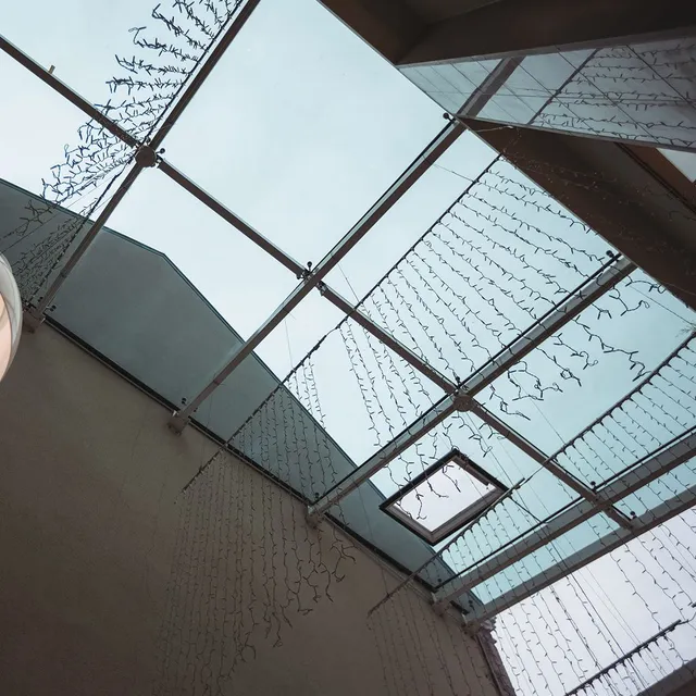 A glass skylight with a metal frame and hanging decorative string lights viewed from below against an overcast sky.