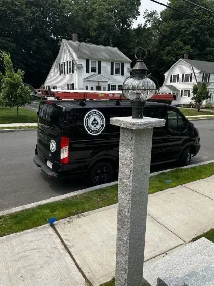 Black van parked on street in front of a white house. Lamp post in foreground.