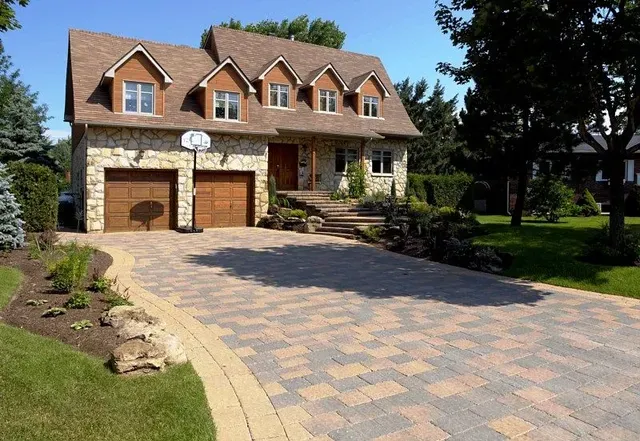 Large stone house with a two-car garage, paved driveway, and landscaped front yard