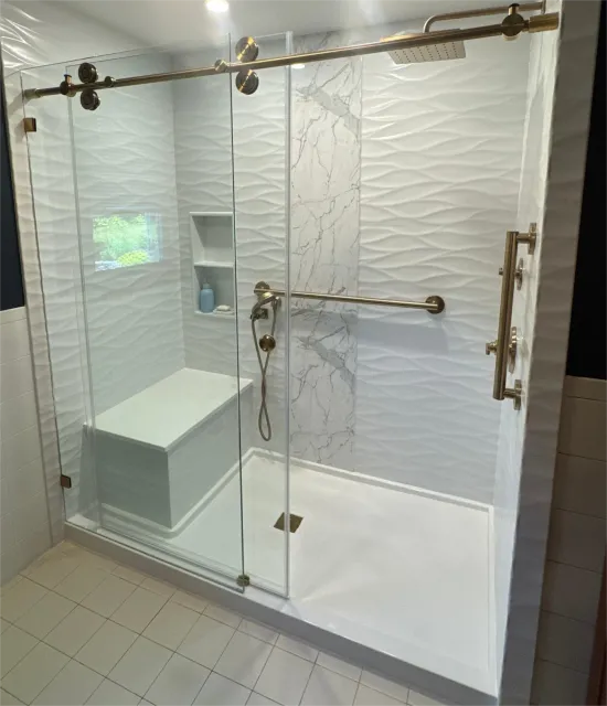 A white shower with a glass door, gold features, and a shower bench.