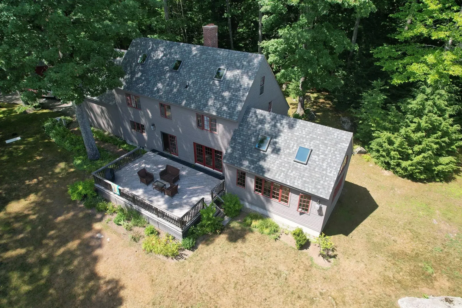 Aerial view of a gray-roofed house with a patio, surrounded by trees and a grassy yard.