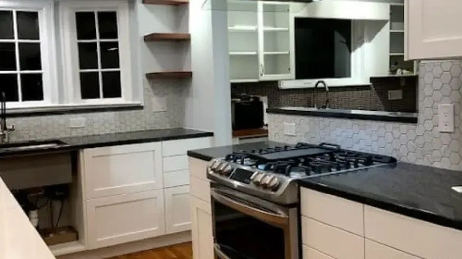 Modern white kitchen with gas range, black countertops, tile backsplash, and open shelving, located in the Greater Boston area