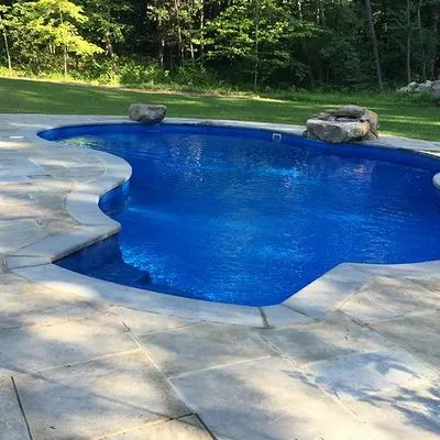 A large blue swimming pool is surrounded by a stone patio.