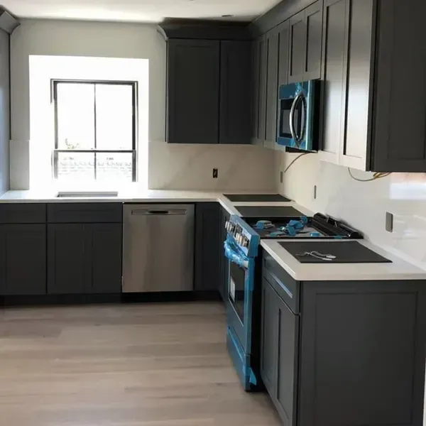 Gray kitchen cabinets, white countertops, stainless steel appliances, and a window.
