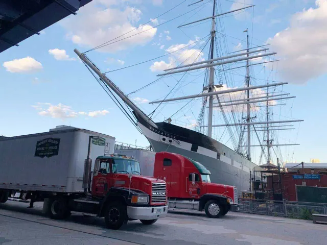 Two trucks are parked in front of a large ship.