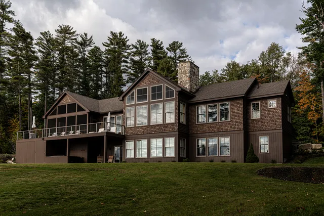 Luxurious brown house surrounded by pine trees under a cloudy sky.