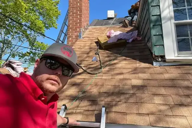 Roof repair technician on a sloped roof with shingles, demonstrating expertise and safety measures, with tools and materials for roofing services visible.