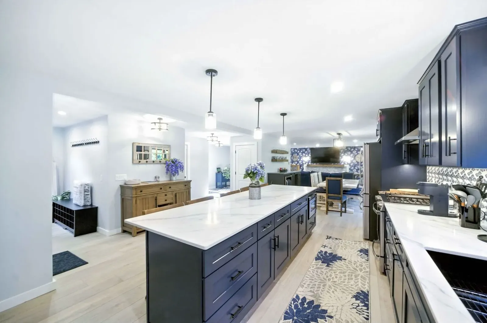 Bright modern kitchen with blue cabinets, white island, pendant lights, and patterned rug