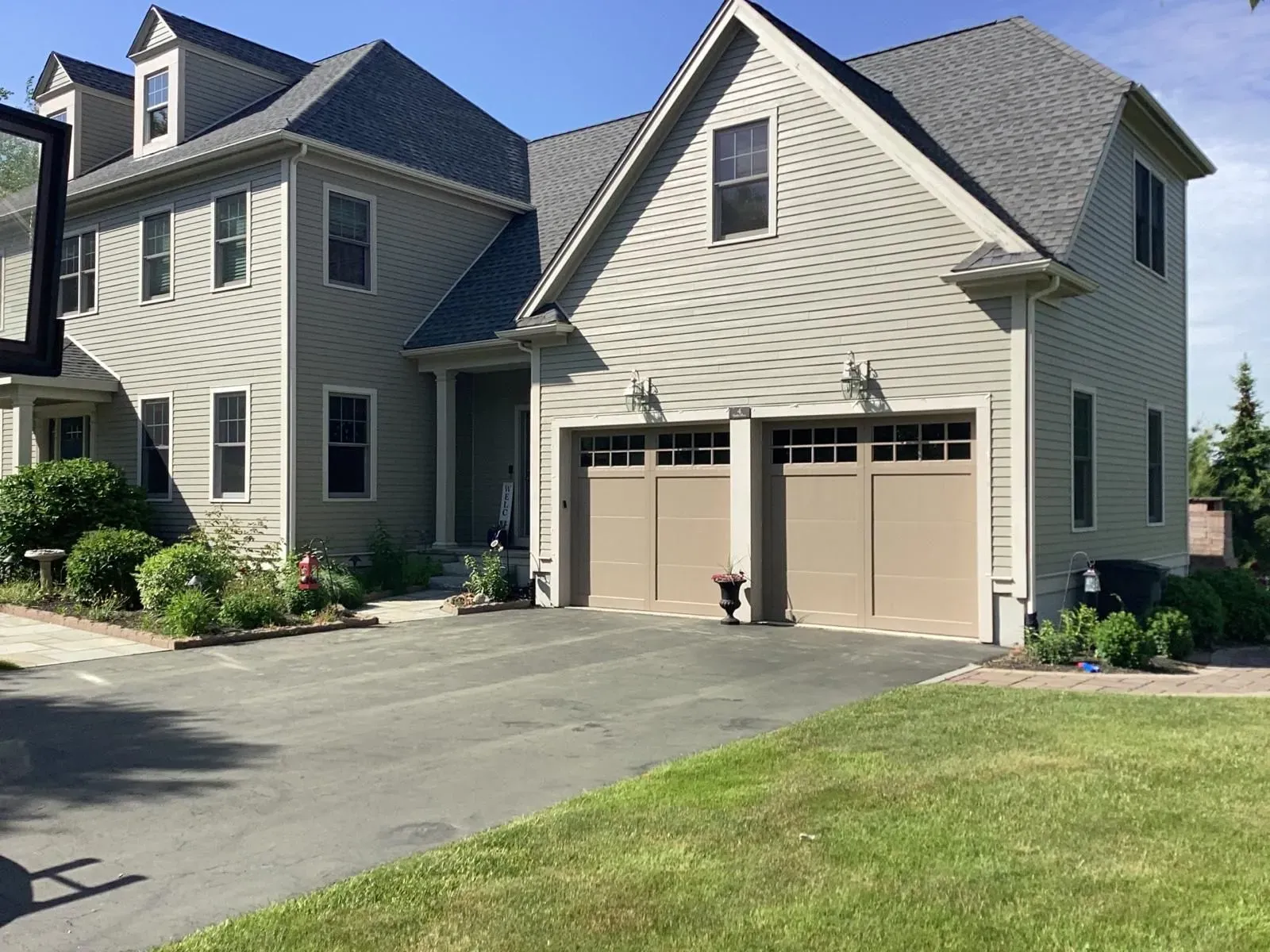 Suburban house with beige siding, two garage doors, driveway, and green lawn on a sunny day