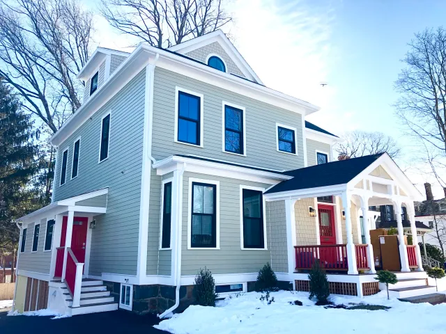 New siding, trim and windows are added to this historic home on Cape Cod with red doors and railings
