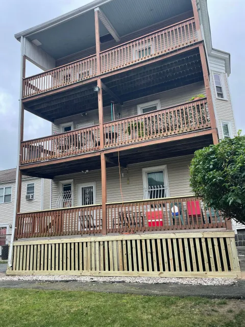 A beige three-story apartment building with stacked wooden porches and a newly built lattice deck base.