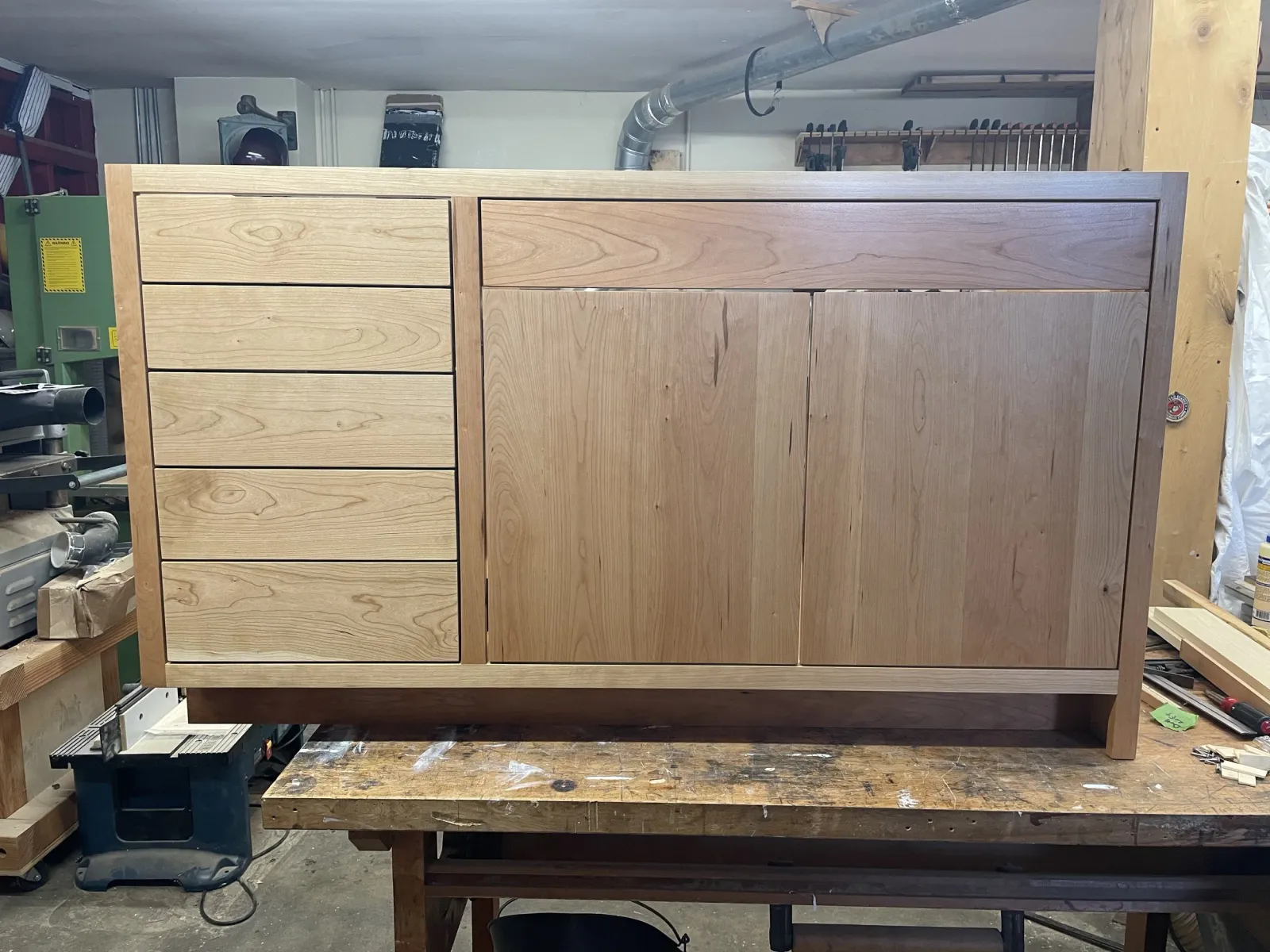 A partially finished wooden cabinet with drawers and doors on a workbench in a woodworking shop.
