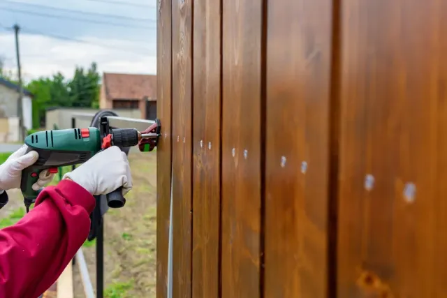 L&L Fences crew member fastening a board on a stained wood fence