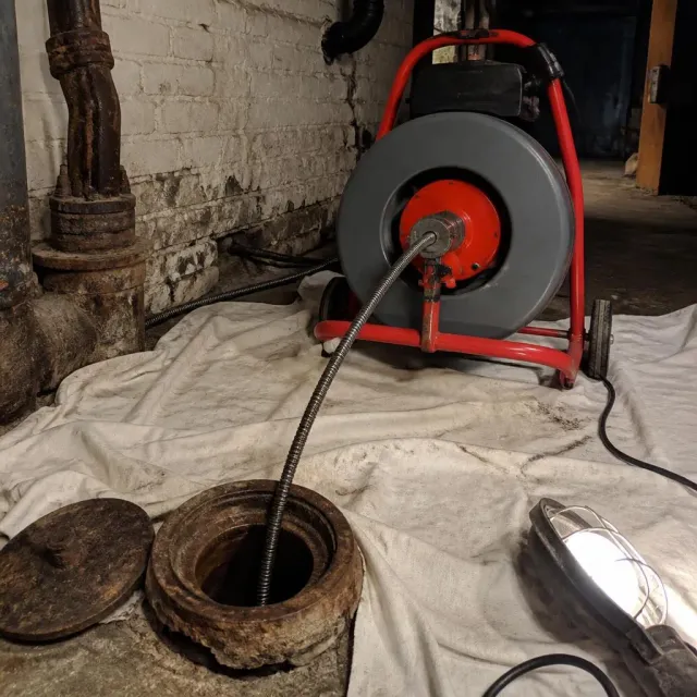 Powered drum auger cabling a cast iron floor cleanout in a basement