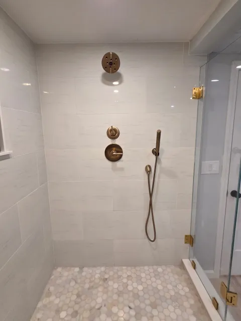Shower with brass fixtures, glass door, and small hexagonal tile floor in a modern bathroom.