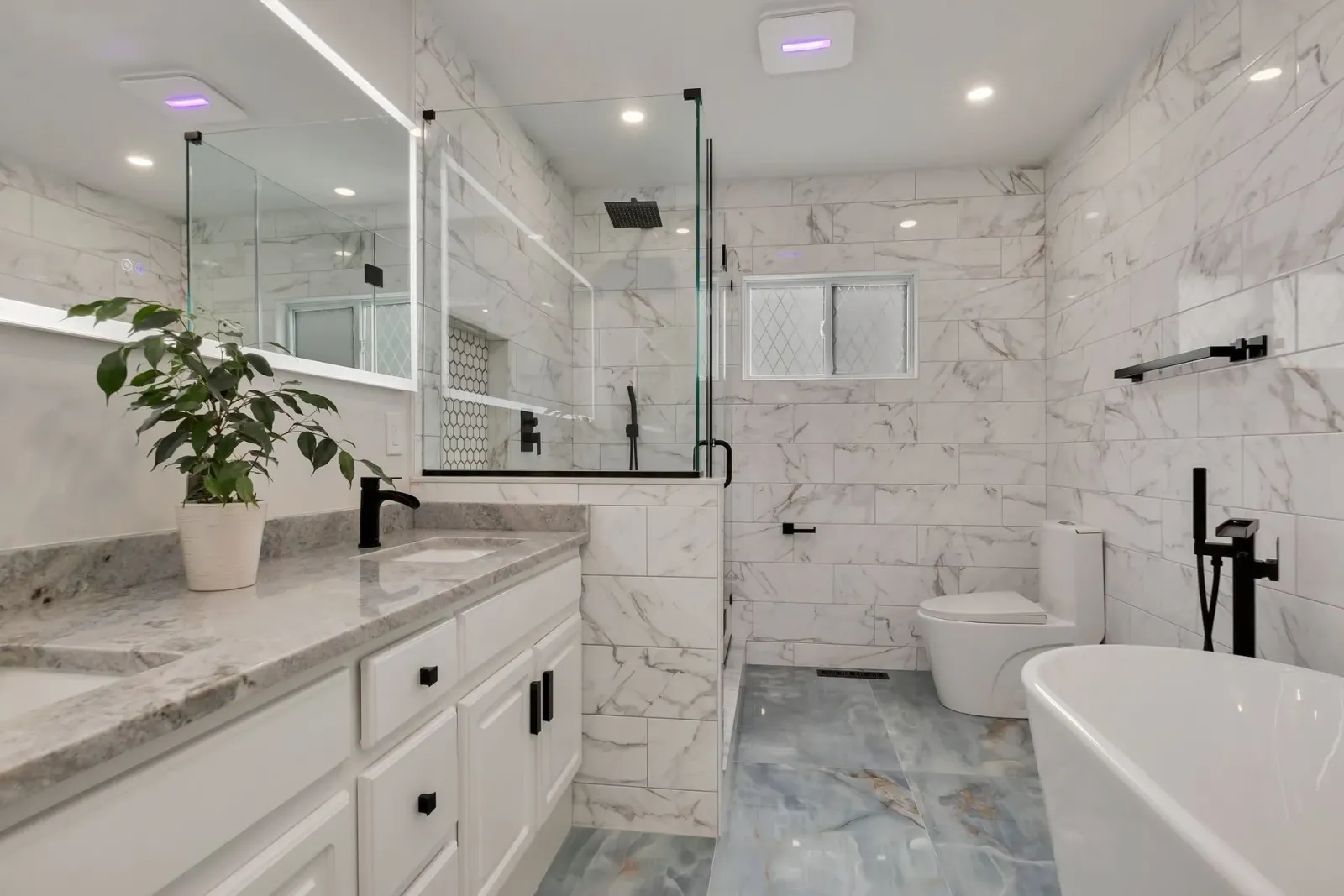 Modern bathroom with marble tile, glass shower, double vanity, and freestanding tub.